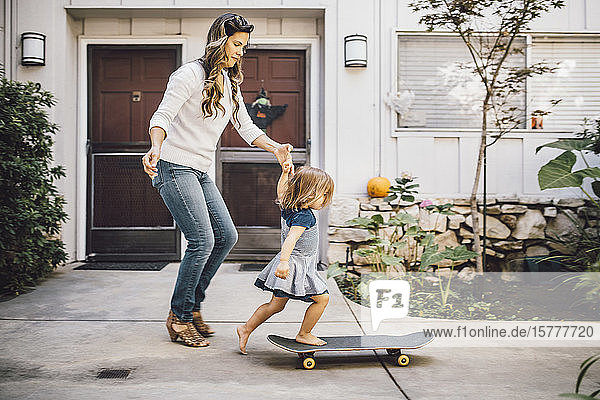 Tochter balanciert über Skateboard mit Hilfe der Mutter auf dem Fußweg