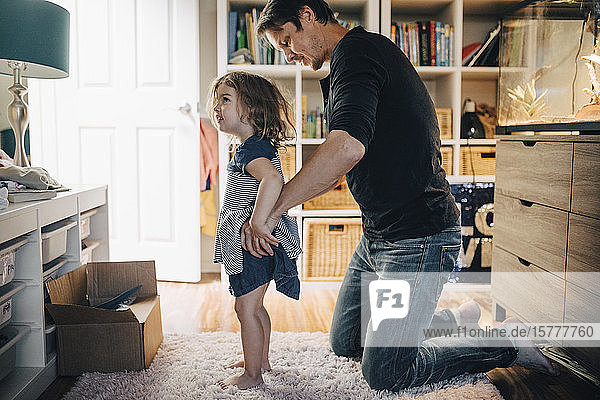 Father dressing daughter in living room