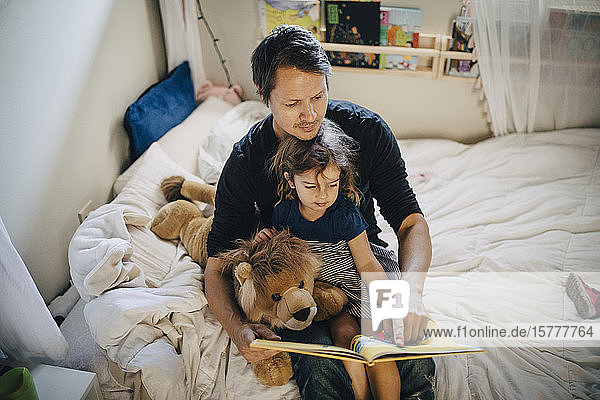 High angle view of father reading book with daughter while sitting in bedroom