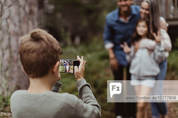 Boy taking picture of family with mobile phone while standing in backyard