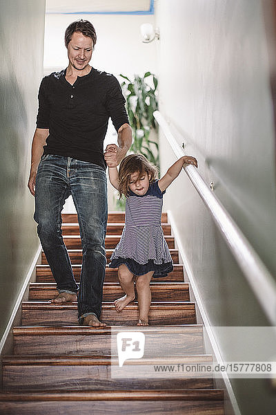 Lächelnder Vater hält der Tochter beim Treppensteigen zu Hause die Hand