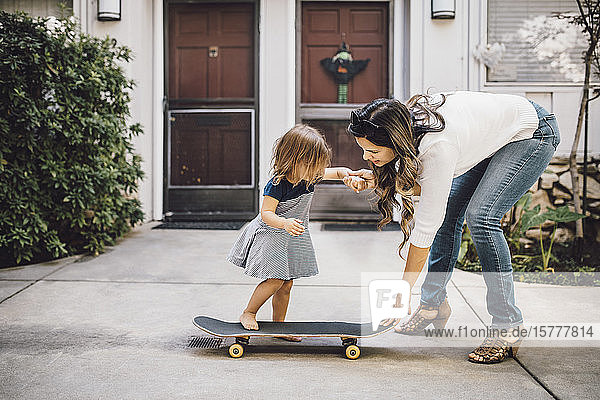 Daughter skateboarding with help of smiling mother on footpath