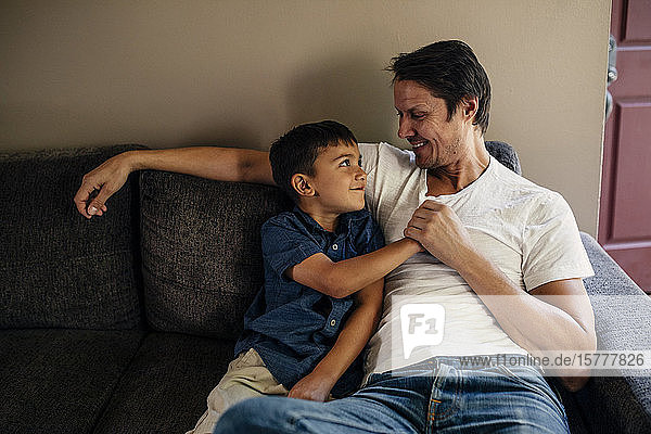 Happy father with son sitting on sofa at home