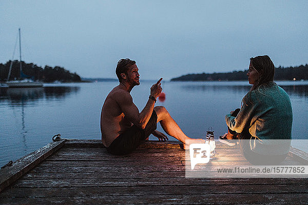 Ehepaar redet in voller Länge  während es auf dem Pier am Meer gegen den Himmel sitzt