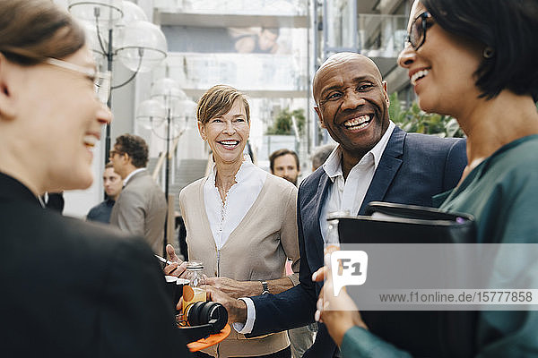 Happy male and female business people talking while standing in office