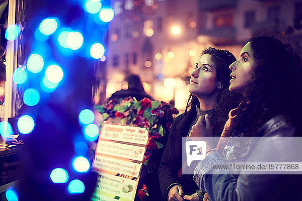 Lesbisches Paar  das sich die Speisekarte ansieht  während es nachts gegen den Konzessionsstand steht