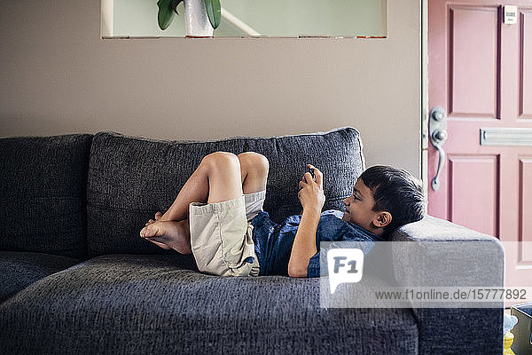 Smiling boy using phone while lying on sofa at home