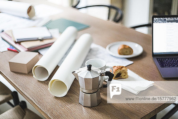Hochwinkelansicht einer Teekanne mit aufgerollten Dokumenten auf dem Tisch