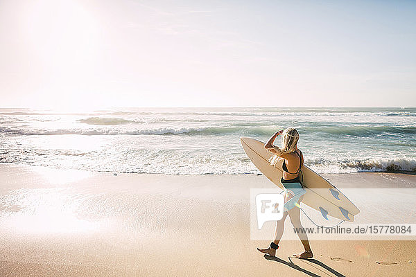 Frau im Neoprenanzug hält Surfbrett am Strand