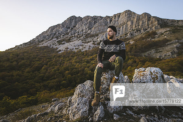 Mann sitzt auf einem Felsen am Berg