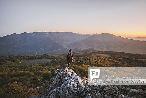 Man on rock by mountains at sunset