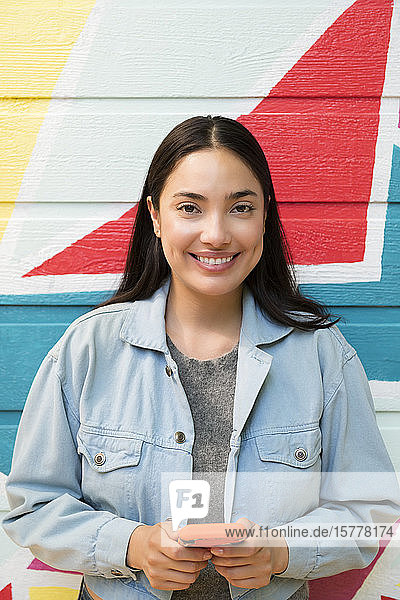Smiling woman holding smart phone against colorful wall