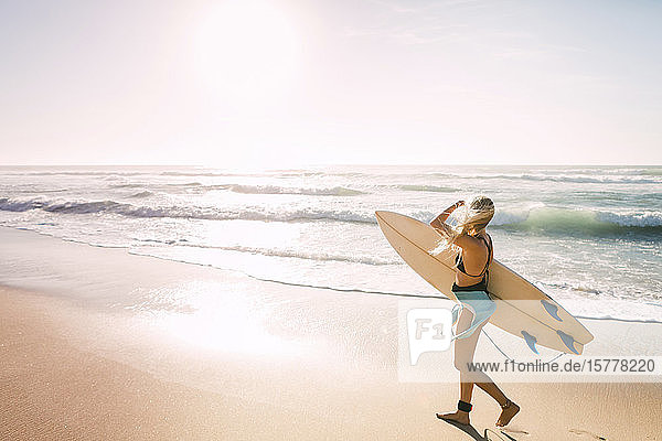 Frau im Neoprenanzug hält Surfbrett am Strand