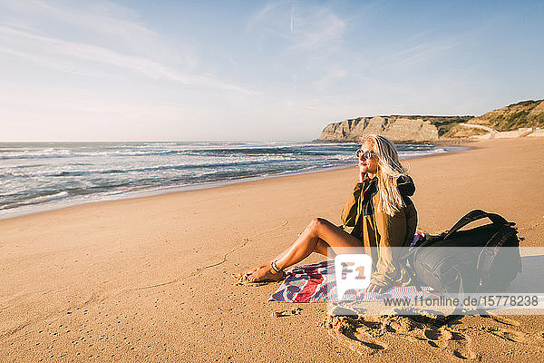 Frau sitzt auf Handtuch am Strand