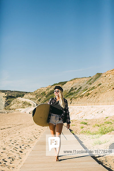 Frau hält Surfbrett auf der Strandpromenade