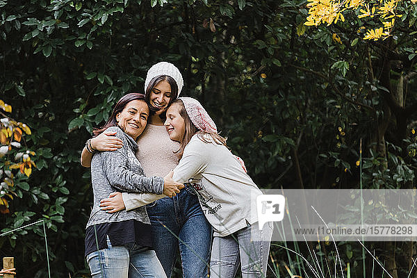 Mother and daughters embracing by trees
