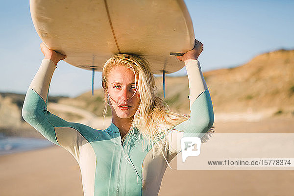 Woman holding surfboard above her head at beach