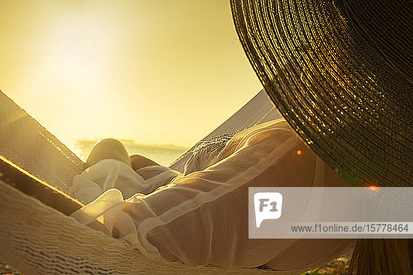 Woman wearing hat on hammock at sunset