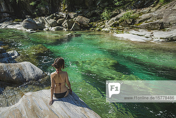 Frau im Bikini sitzt auf einem Felsen am Fluss
