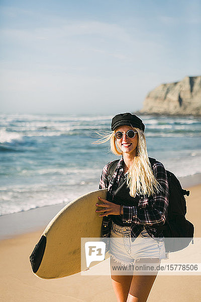 Smiling woman holding surfboard on beach