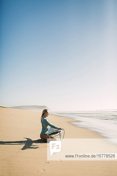 Frau kniend mit Surfbrett am Strand