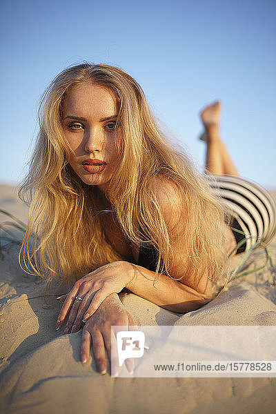 Blonde Frau auf Sand liegend