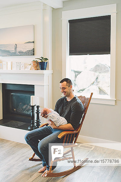 Father sitting in rocking chair holding newborn baby boy