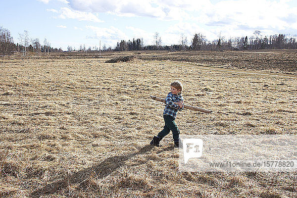 Boy carrying wooden pole across field