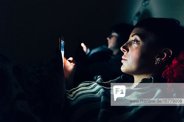 Frauen im Bett in der Dunkelheit mit Mobiltelefonen