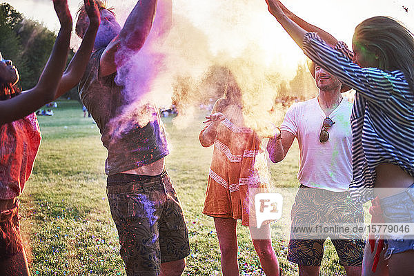 Fünf junge erwachsene Freunde tanzen und werfen farbiges Kreidepulver auf das Holi-Fest