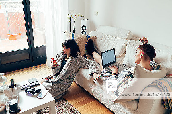 Frauen entspannen sich auf dem Sofa mit Laptop und Mobiltelefon
