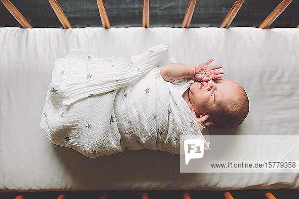 New born baby boy swaddled in cot overhead view