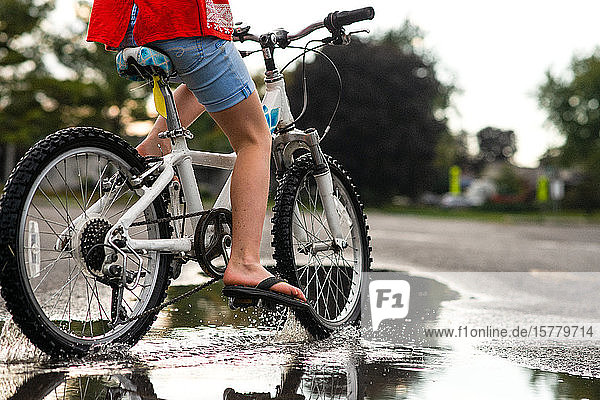 Mädchen fährt Fahrrad auf nasser Straße