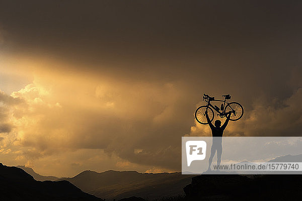 Radfahrer hebt Fahrrad gegen Sonnenuntergang am Berg