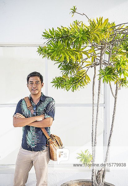 Man with arms crossed standing beside thin green plant