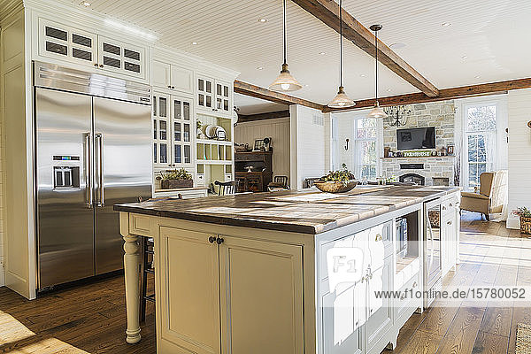 Interior view of country style open plan kitchen with kitchen island and stained oak wood floorboards inside home Quebec Canada.