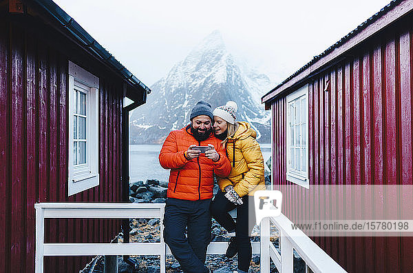 Touristenpaar mit Smartphone auf einer Veranda auf Hamnoy Lofoten Norwegen