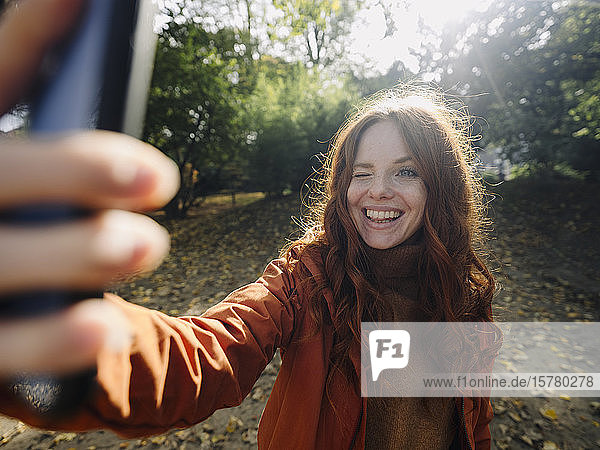 Glückliche rothaarige Frau  die im Herbst in einem Park ein Selfie macht