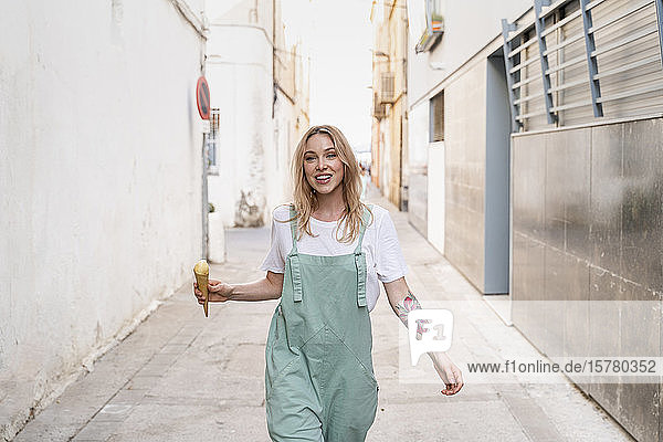 Porträt einer glücklichen jungen Frau mit Eistüte  die eine Gasse entlang läuft