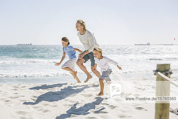 Vater amüsiert sich mit seinen Söhnen am Strand  rennt und springt im Sand