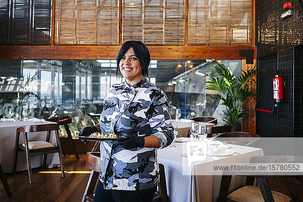 Portrait of smiling woman serving a dish in restaurant