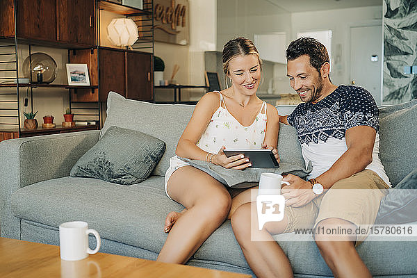 Glückliches  entspanntes Paar sitzt auf einer Couch im Wohnzimmer und teilt sich eine Tafel