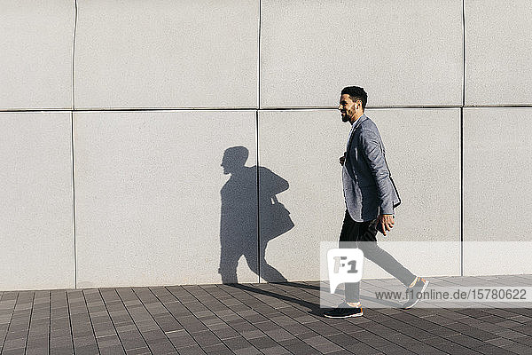 Casual young businessman walking along the wall in the city