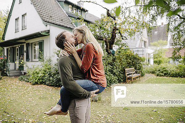 Happy couple kissing in garden  in front of their dream house