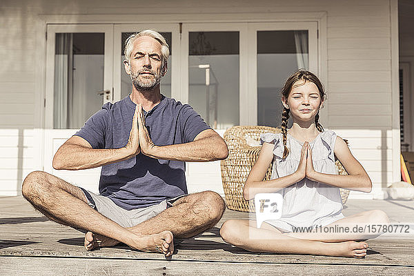 Vater und Tochter sitzen bei Sonnenschein auf der Terrasse und machen Yoga
