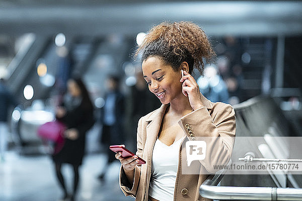 Lächelnde junge Frau mit Handy und Ohrstöpseln in der U-Bahn-Station
