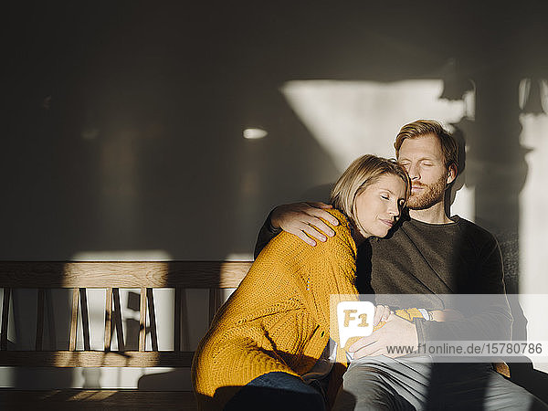 Entspanntes Paar  das zu Hause im Sonnenlicht auf einer Bank sitzt