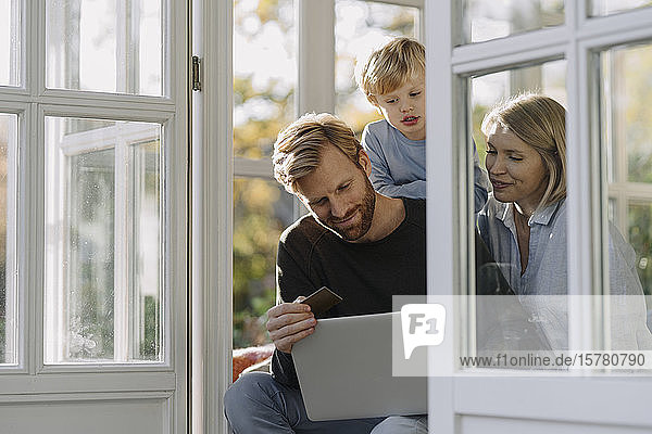 Familie mit Laptop und Kreditkarte im Wintergarten zu Hause