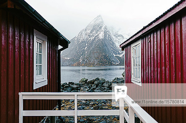 Rote Hütten und schneebedeckter Berg an der Küste  Hamnoy  Lofoten  Norwegen