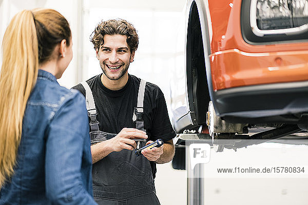Glücklicher Automechaniker im Gespräch mit Kunden in der Werkstatt